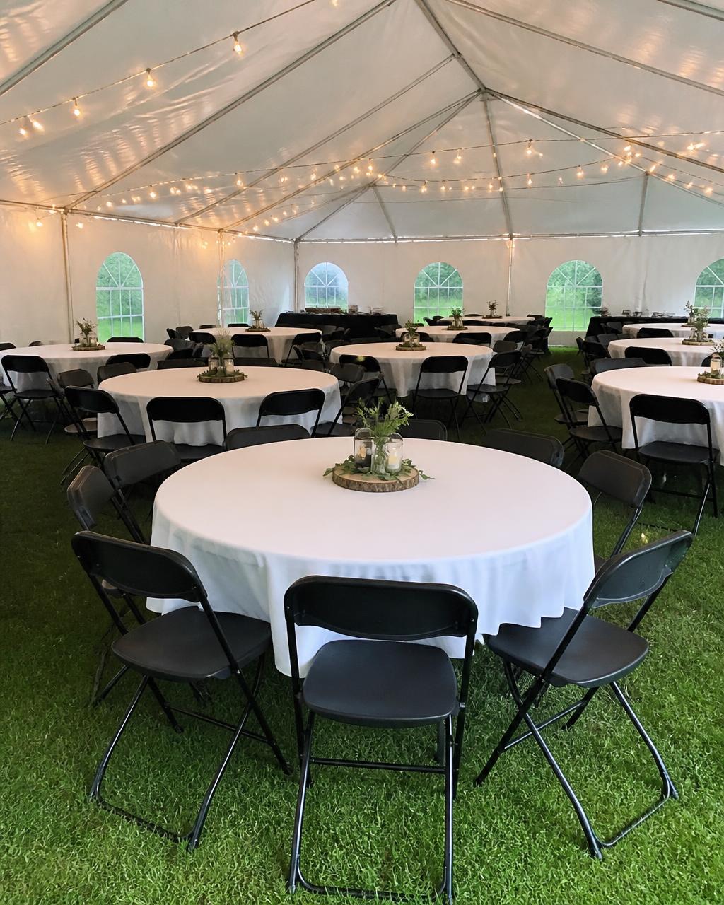 Black folding chairs around round banquet tables under a white event tent